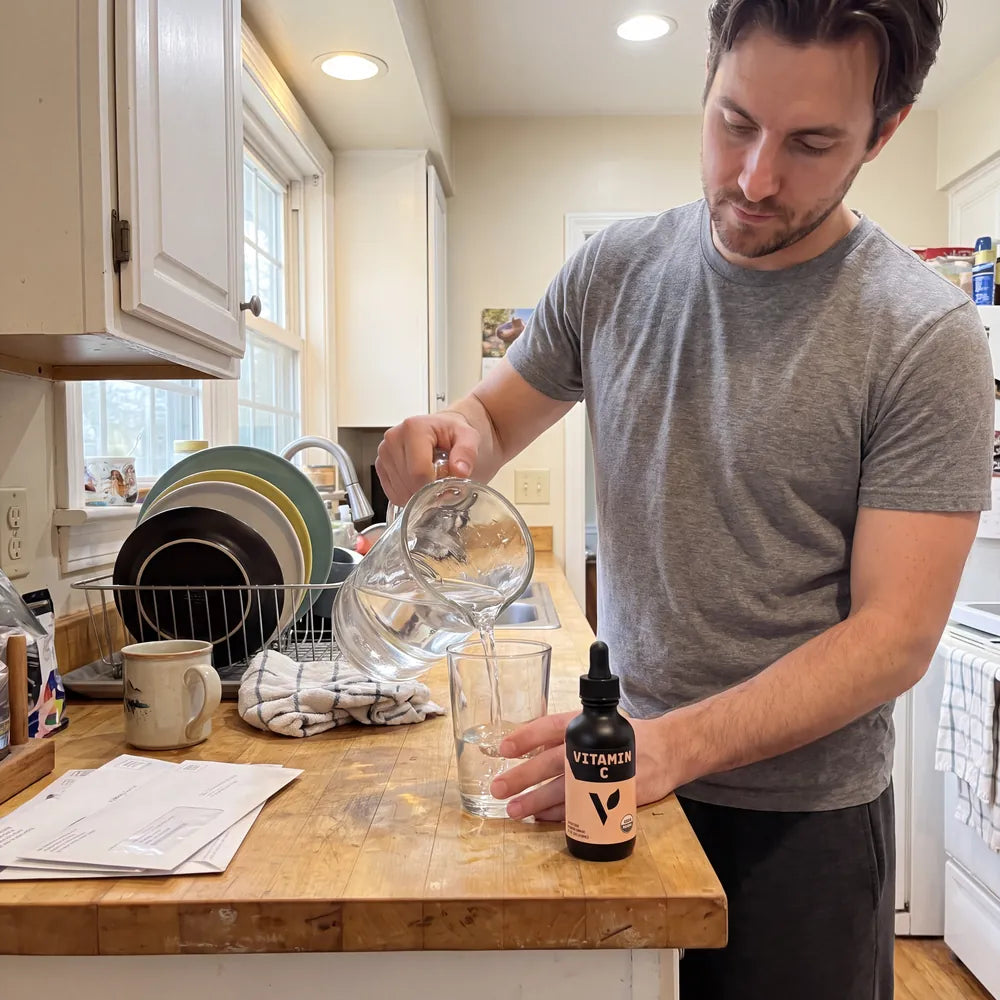 Man pouring water into a glass beside the Organic Vitamin C bottle